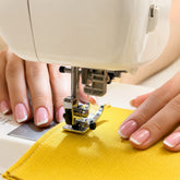 Manos trabajando en una máquina de coser durante la creación artesanal de una pieza textil de SimLi en el taller.
