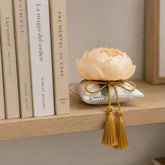 Decoración textil Alba Peonía sobre estantería de madera junto a libros de hogar y decoración.