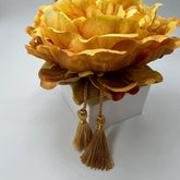 Adorno floral hecho a mano con peonía artificial amarilla, diseñado para ser perfumado. Colocado sobre un pedestal mostrando sus borlas, es ideal para decorar y ambientar estanterías.