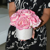 Arreglo de rosas artificiales rosas y crema en una caja redonda blanca, sostenido con ambas manos para mostrar su tamaño y volumen