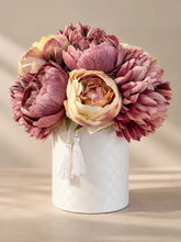 Centro de mesa con flores artificiales en tonos rosa y crema, presentado en un jarrón cilíndrico blanco con acabado textil y borlas decorativas