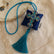 Colgante decorativo artesanal Cruz de Amalfi de SimLi Atelier sobre tejido bordado, con cruz de cristales azules y borla textil