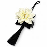 Detalle de Jazmín de Moraira, colgante decorativo artesanal SimLi con flor blanca sobre cojín negro y borla textil.