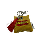 Vista frontal de un llavero amarillo con bandera de España formada por cristales rojos y amarillos y borla roja.