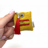 Detalle de un llavero decorativo amarillo con motivo de la bandera española en cristales y borla roja.