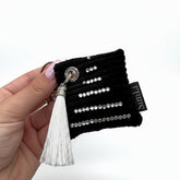 Llavero decorativo negro con cristales plateados y borla blanca sostenido en la mano.