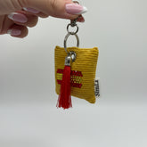 Llavero amarillo con cristales de la bandera de España y borla roja mostrado colgado por el mosquetón
