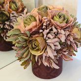 Rosas y crisantemos artificiales en tonos rosa, verde y malva sobre una base decorativa burdeos