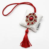 Detalle frontal del colgante textil Rubí de Granada de terciopelo blanco con cordón rojo, borla decorativa y broche de cristales rojos
