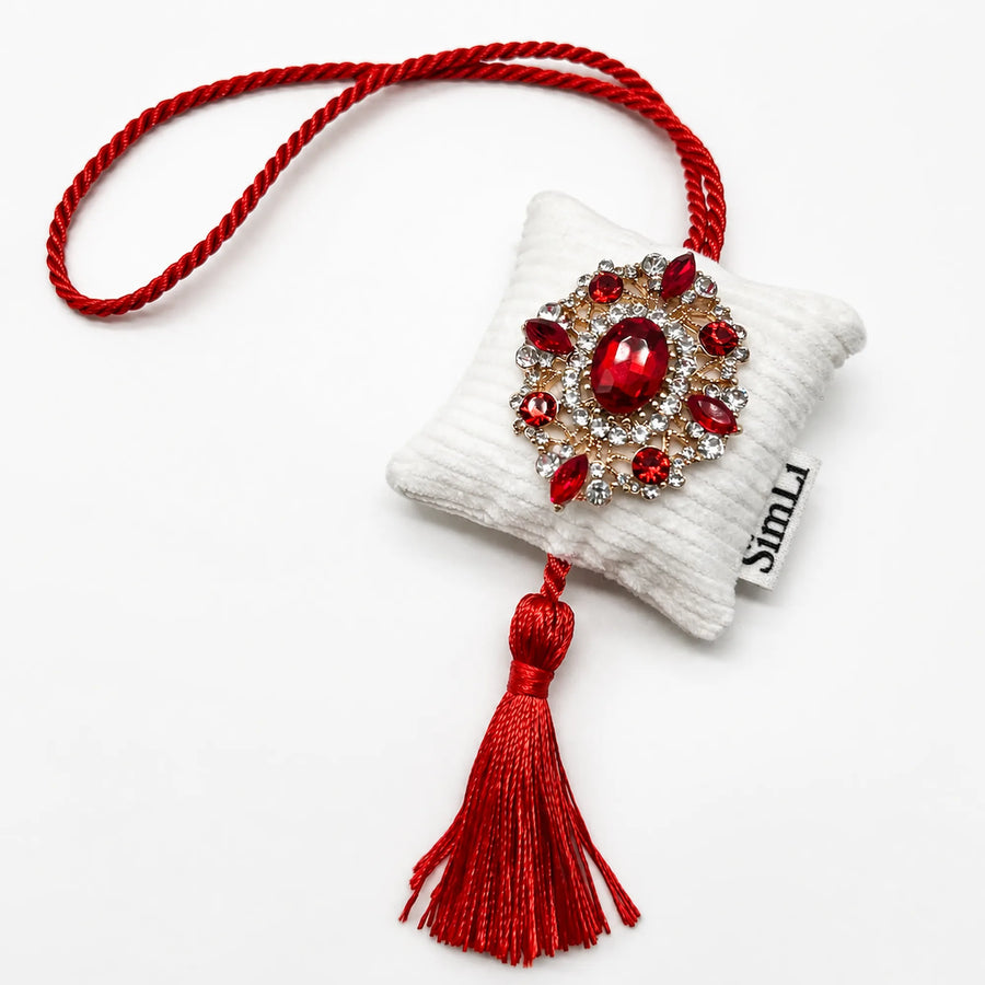 Detalle frontal del colgante textil Rubí de Granada de terciopelo blanco con cordón rojo, borla decorativa y broche de cristales rojos